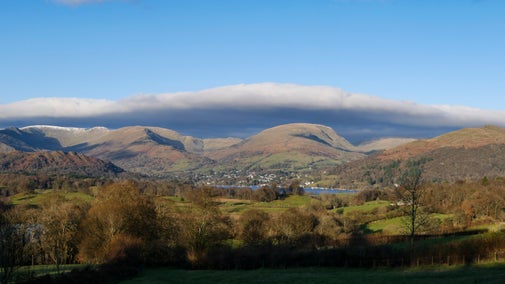 View looking over Blelham Tarn towards Ambleside, Red Screes and Fairfield, Cumbria, including trees with autumn foliage in the foreground, the blue water of the tarn, a dusting of snow on the hills, and low cloud